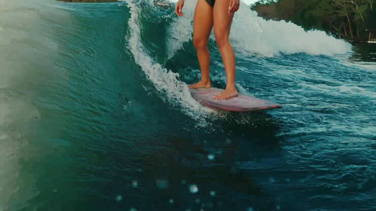 Female wake surfer's legs on pink board surfing perfect wave on lake in slow motion