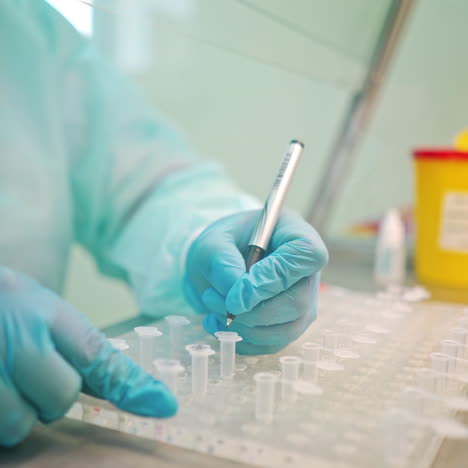 laboratory worker writes with a pen on test tubes. hands in blue protective gloves writing on plastic vials on the table indoors. close-up.