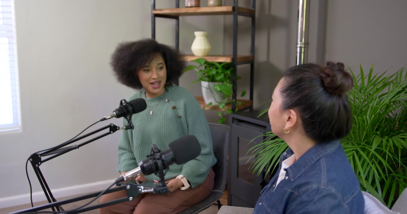 Donne asiatiche e afroamericane che registrano, parlano e gesticolano con microfoni durante un'intervista in studio.