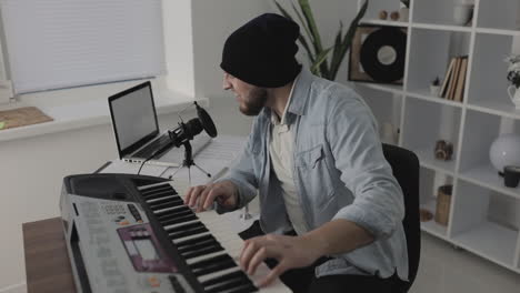 male musician singing, playing electric keyboard and using a laptop at home 1