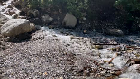 Idyllic-small-waterfall-flowing-down-the-rocky-mountains-in-summer---panning-shot-slow-motion