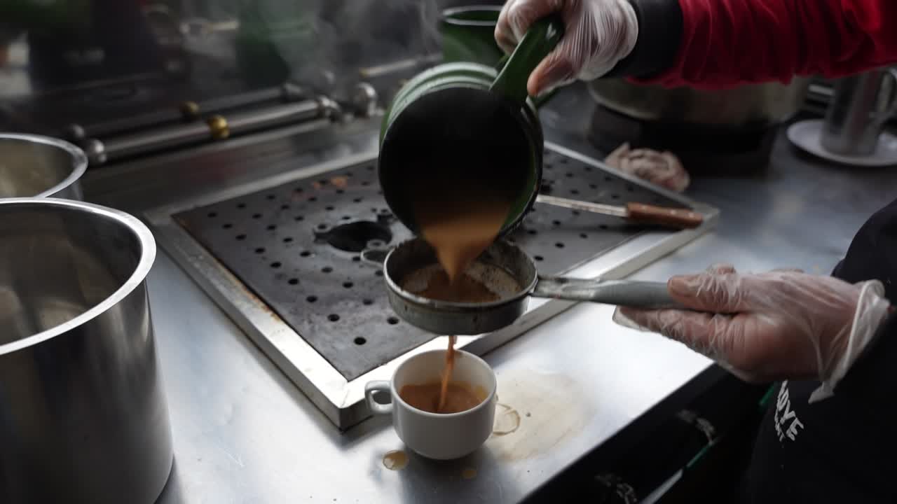 Gloved hand pours spiced tea through a strainer into a cup at a street-side setup