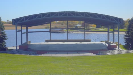 a man walks onto an empty stage at an outdoor park amphitheater on a beautiful sunny day