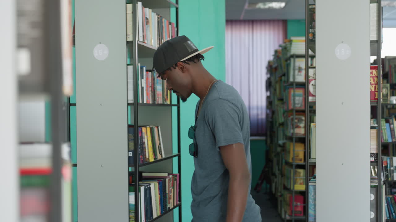 Wide library aisle view with books on shelves left and right as student walks past, exploring stacks quietly, soft focus bokeh, calm study mood, teal walls