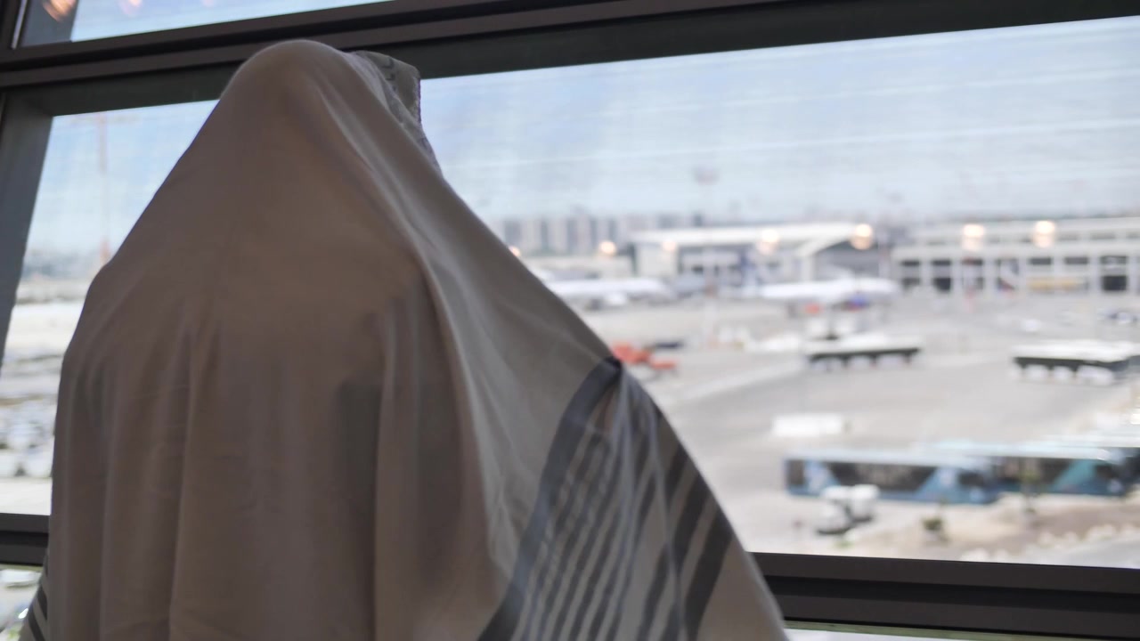 Un uomo ebreo che si copre con un Talit per pregare all'aeroporto di fronte al terminal.