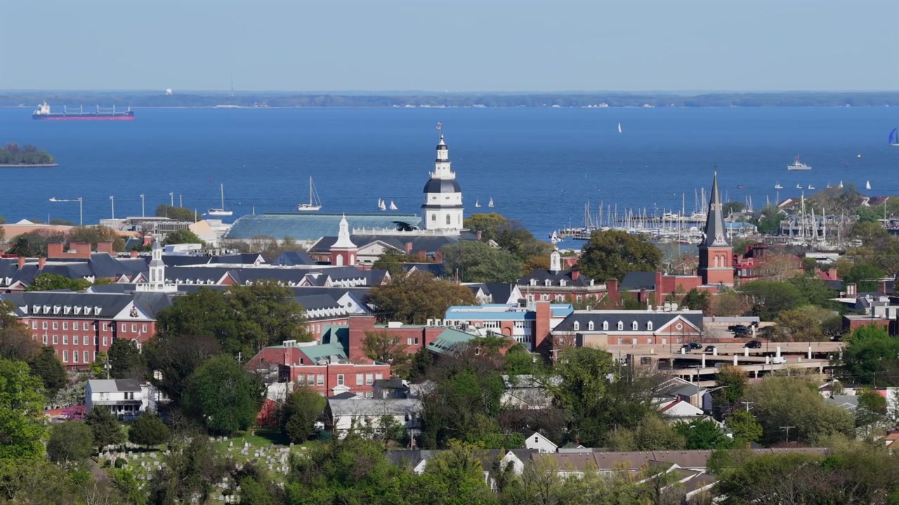 Ampia veduta aerea di Annapolis, Maryland, sotto il sole primaverile con lo skyline storico della città, campanili, barche nel porto turistico e le calme acque blu della Baia di Chesapeake sullo sfondo. Vista panoramica