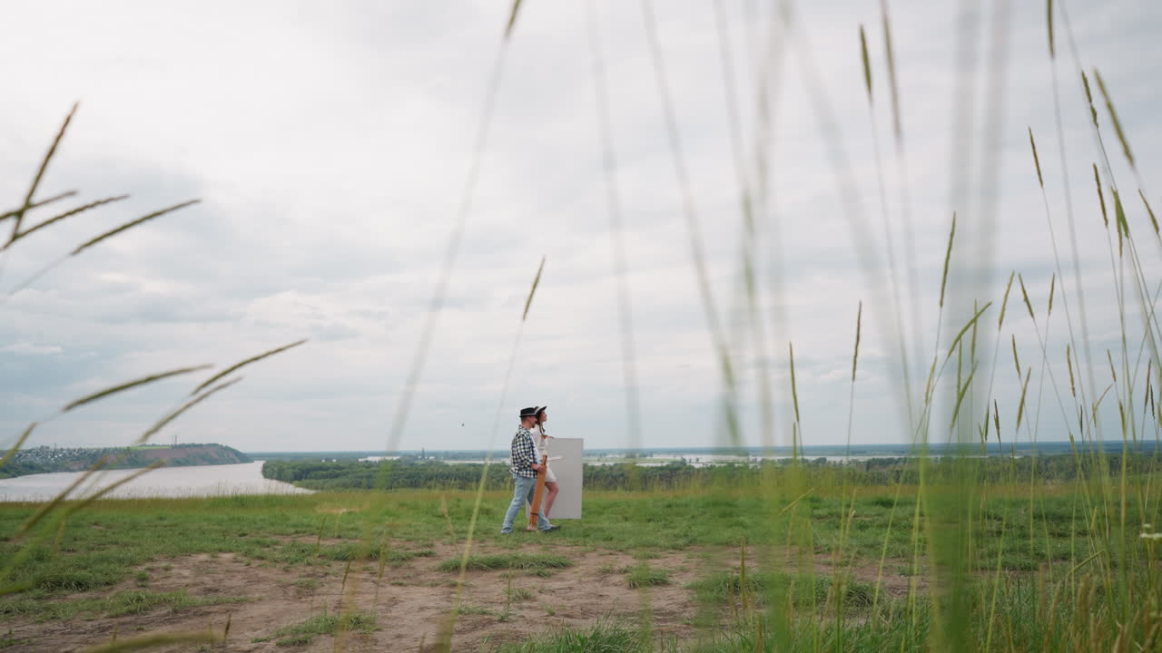 예술가들은 앞에 있는 경치 좋은 풍경을 그릴 준비가 되어 있는 스과 캔버스를 들고 을 고 있다. 그 남자는 어두운 모자를 은 색 셔츠를 입고 있다.