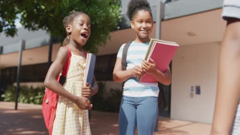 Video-of-three-happy-diverse-schoolchildren-with-schoolbags-greeting-outside-school
