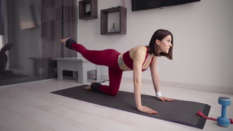 woman in sportswear practicing donkey kick exercise with ankle weight, raising one leg up