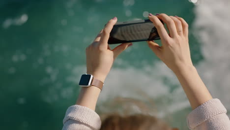 woman using smartphone taking photo of ocean legs dangling over water barefoot sharing summer vacation on social media watching waves