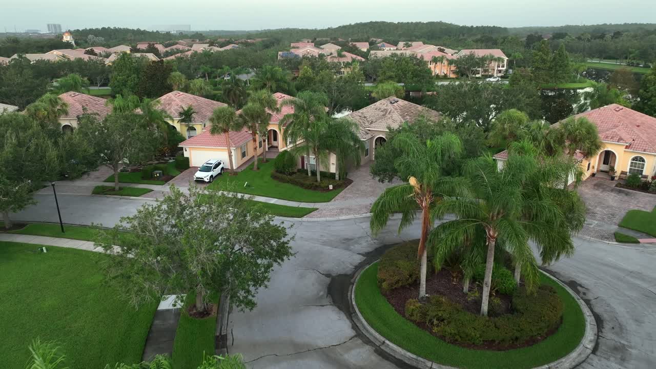 Aerial view of residential neighborhood in Florida, with well-manicured lawns, palm trees and Mediterranean-style homes. Circular driveway in charming community, surrounded by lush greenery