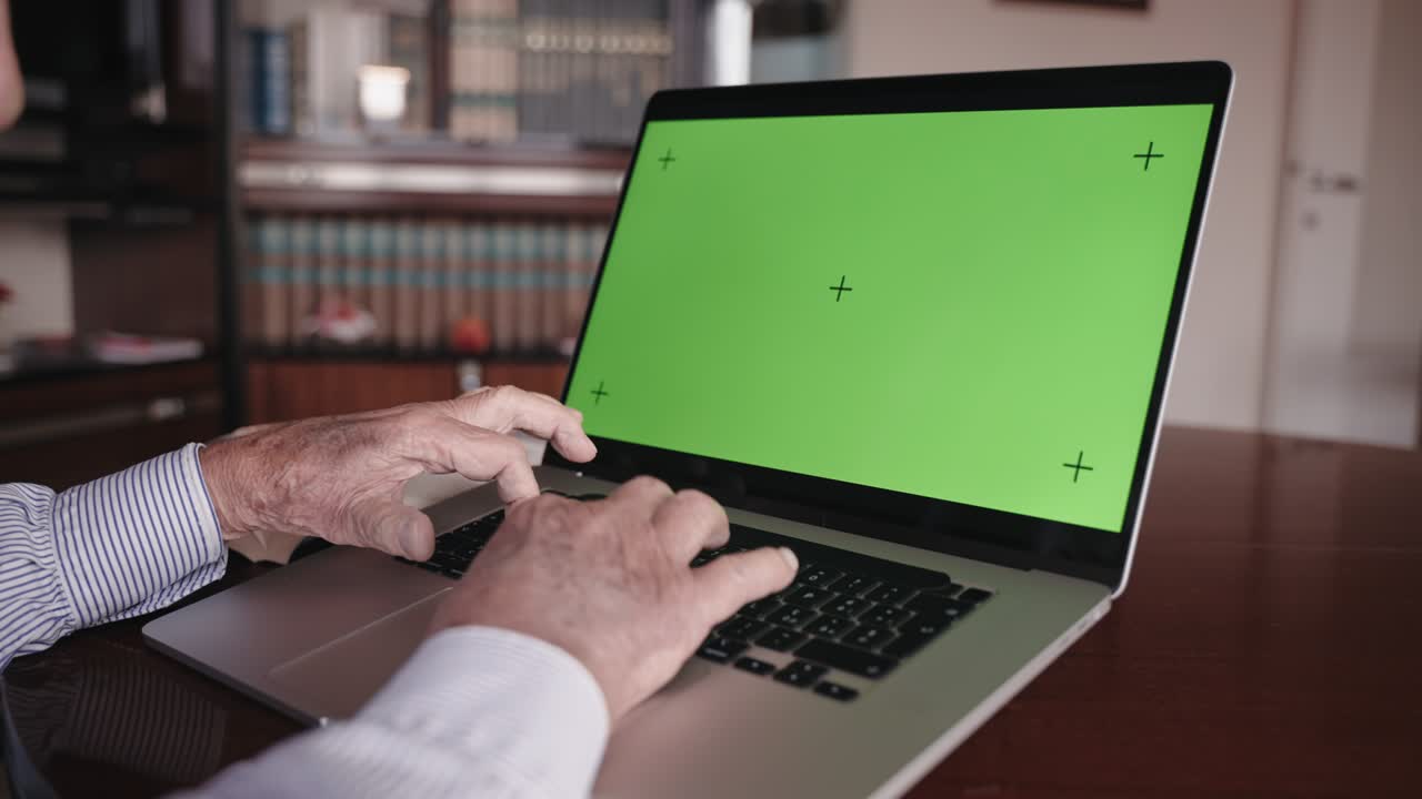 manos arrugadas del profesor sénior atando en el teclado de la computadora con maqueta de pantalla verde, anciano jubilado trabajando en un dispositivo de moda en la oficina de casa. manos del hombre sénior escribiendo proyecto en portátil