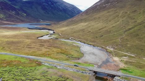 panning drone shot of car driving over bridge in mountain valley landscape