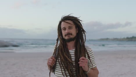 close up portrait of young confident man with dreadlocks smiling cheerful at beach