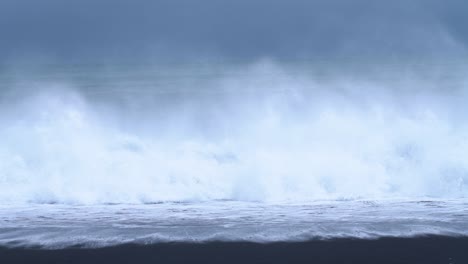 strong waves crashing onto the shore at black sand beach in iceland