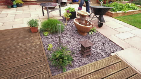 footage of man working in garden, getting slate out of a wheelbarrow and throwing it on the ground in a new area