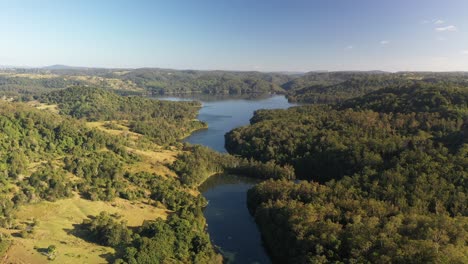 Aerial-shot-of-a-lake-reservoir-of-water-with-forest-surrounding-it-at-sunrise-in-Queensland,-Australia