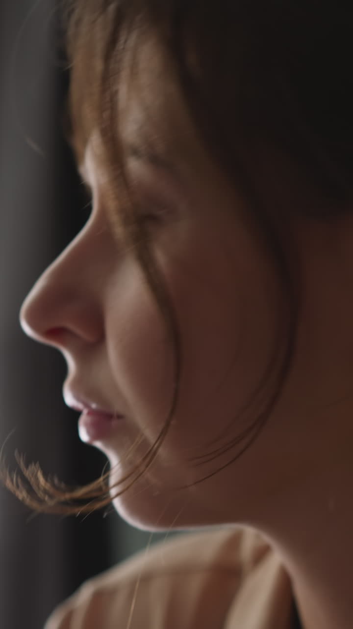 Young woman contemplates in light window sitting in house. Pensive lady turns head and looks at camera calmly. Peaceful female person rests at home