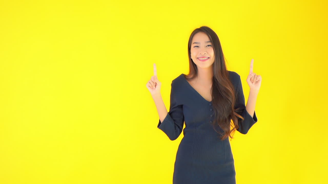 Happy Asian Woman Pointing With Fingers Up. Isolated on Yellow Screen Background