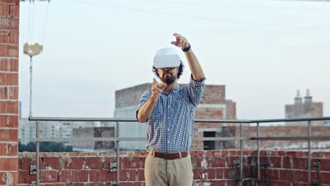 kaukasischer gutaussehender junger architekt oder vorarbeiter in vr-brille steht auf dem dach der baustelle und hat ein headset, als würde er eine virtuelle tour durch die zukünftige architektur beobachten. im freien. neue moderne technologien.