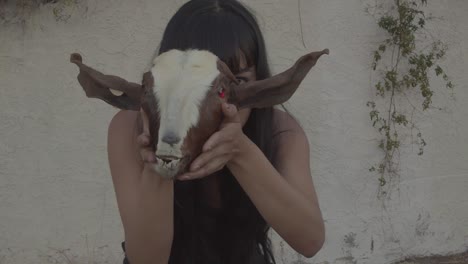 a young woman holding a goat head prop with red eyes