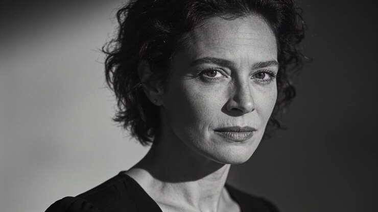 Facing woman shifting gaze with camera rolling in studio, directional light, dark top, stud earring