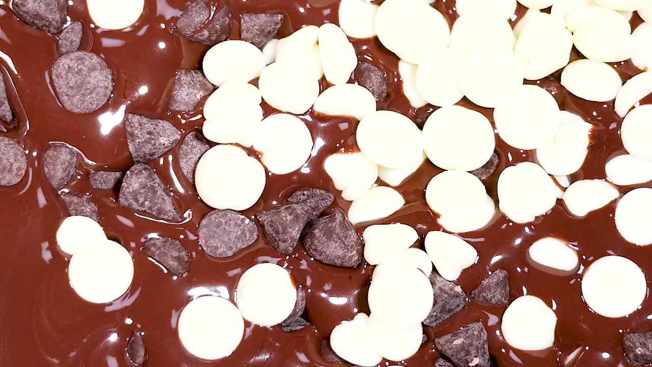 A detailed view of white and dark chocolate chips scattered on a melted chocolate surface.