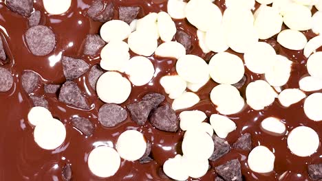 a detailed view of white and dark chocolate chips scattered on a melted chocolate surface.