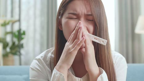 close up single sad woman holding a pregnancy test sitting on a couch in the living room at home