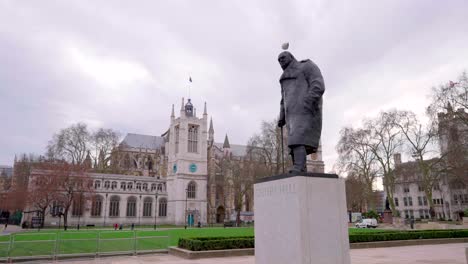 Winston-Churchill-statue-in-London-Parliament,-a-bird-is-nesting-on-his-head,-on-a-cloudy-day