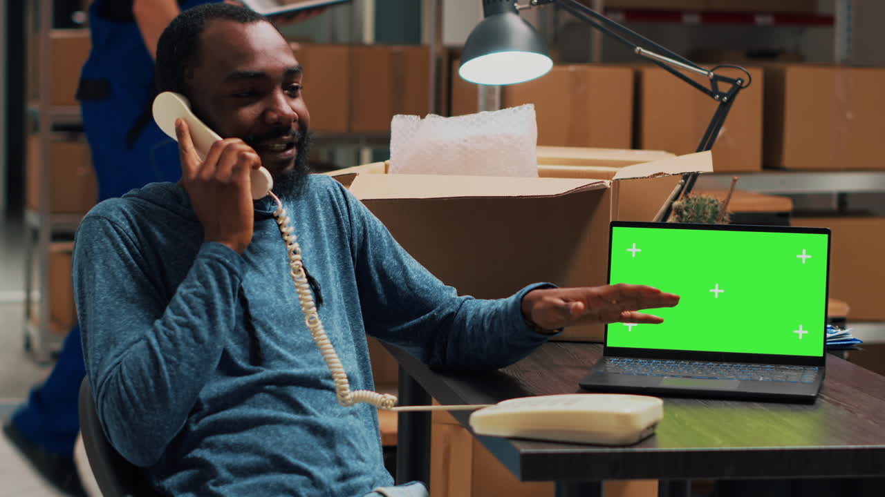 Man talking on phone with green screen laptop in warehouse