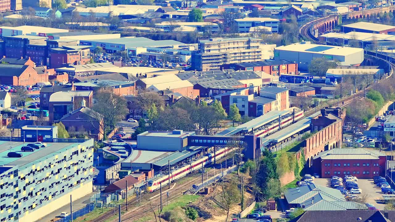 Aerial view of a train arriving at Wakefield station, surrounded by industrial urban buildings, roads, and moving traffic.