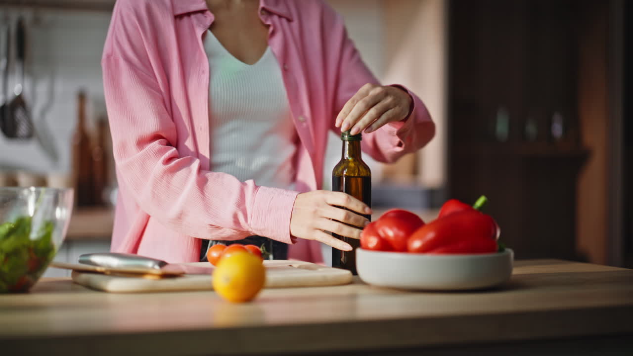 Primer plano de unas manos femeninas echando aceite de una botella en una ensalada en la cocina. Mujer cocinando