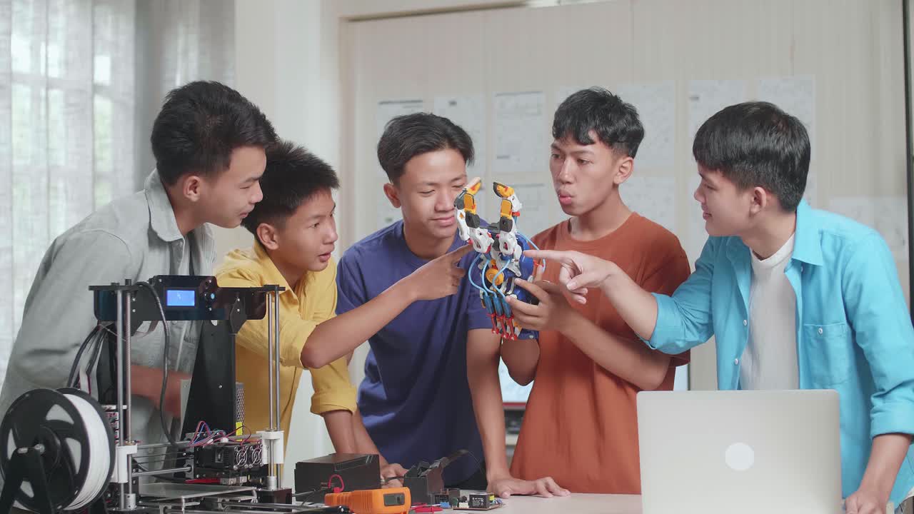 노트북과 3d 프린팅을 가진 젊은 아시아 소년 그룹이 사이보그 손을 확인하고 집에서 일하는 성공을 축하합니다.