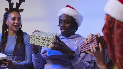 fotografía de estudio de amigos de la generación z dando y abriendo regalos de navidad sentados en el sofá con sombrero de papá noel y cuernos de reno