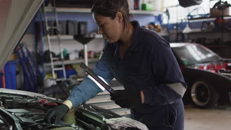mecánica femenina usando una lámpara led y reparando un coche en una estación de servicio de coches