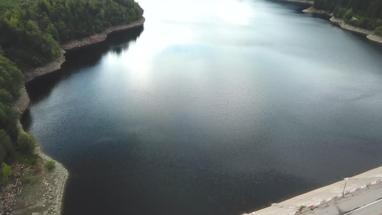 높은 각도, 흐린 날에 댐과 호수 위로 드론 샷을 기울입니다.