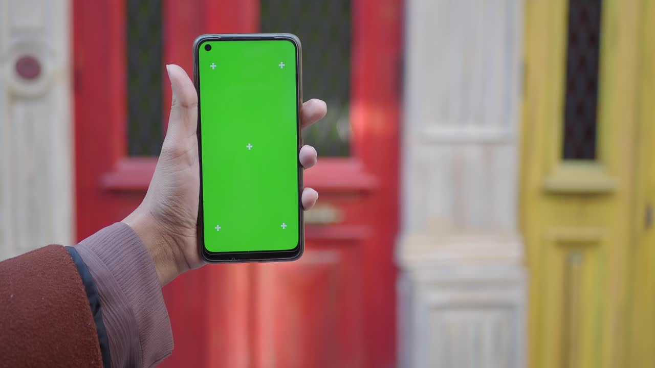 persona sosteniendo un teléfono con una pantalla verde frente a una puerta roja y una puerta amarilla