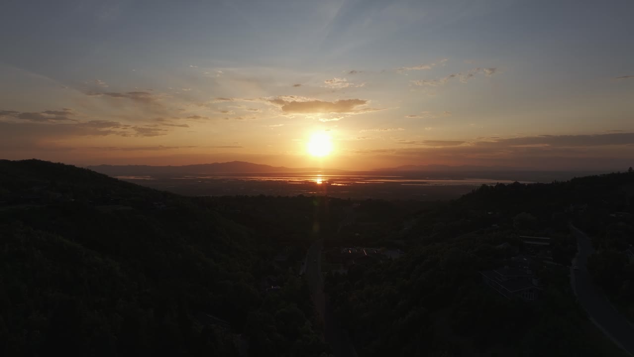 Aerial drone dolly out shot from Bountiful Canyon in Utah at golden hour with road, forest, valley homes, Wasatch Mountains, cityscape, and the Great Salt Lake at sunset
