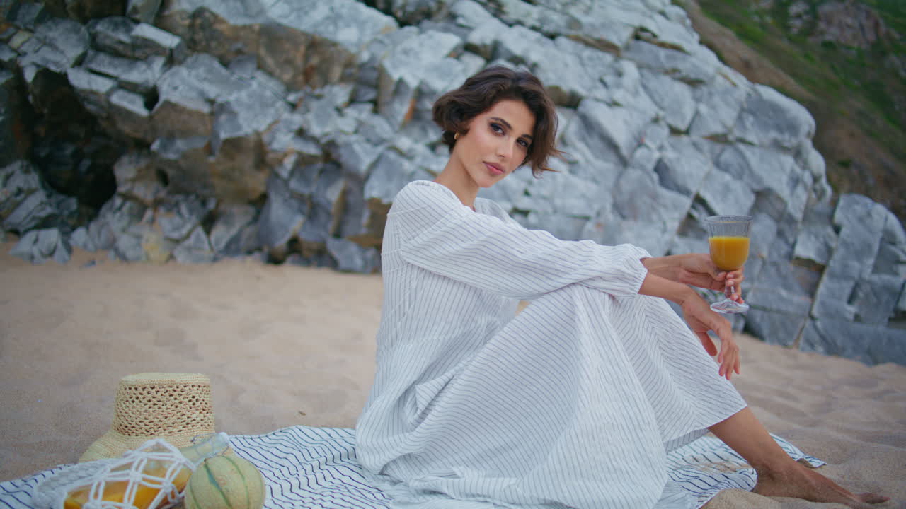 una mujer elegante relajándose en un picnic junto al mar. una hermosa dama posando sosteniendo jugo