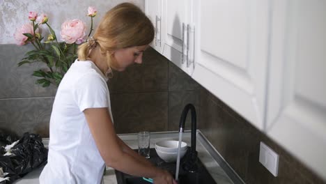 Young-pretty-housewife-washing-dishes-in-modern-kitchen-and-talking-to-someone.-FHD-shot