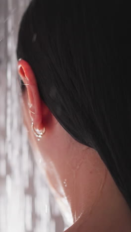 lady with golden earnings stands in shower. woman enjoys hot water flows down body in shower. woman doing bathroom hygienic procedure under hot water