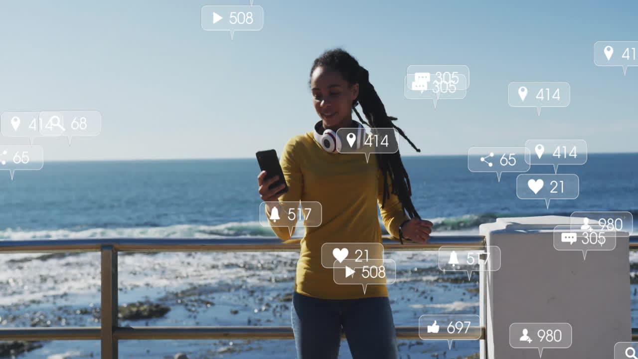 Social media interaction icons animation over woman using smartphone by ocean