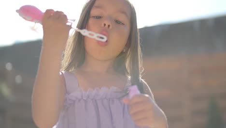 una niña con un vestido está soplando burbujas de jabón en el patio trasero en un soleado día de verano