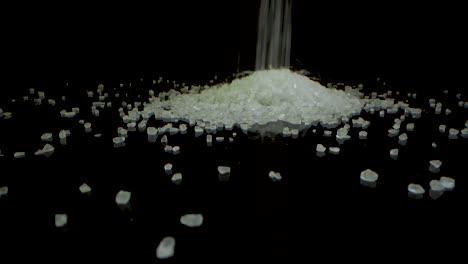 crystal coarse sea salt falling and making a hill on a black mirrored surface