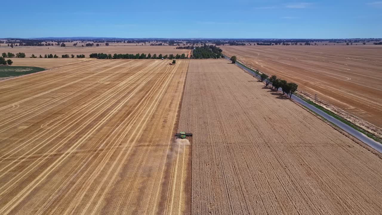 Descending aerial view of a harvester working in a paddock with farmland and hills beyond