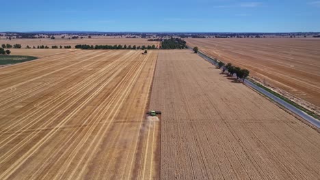 Descending-aerial-view-of-a-harvester-working-in-a-paddock-with-farmland-and-hills-beyond