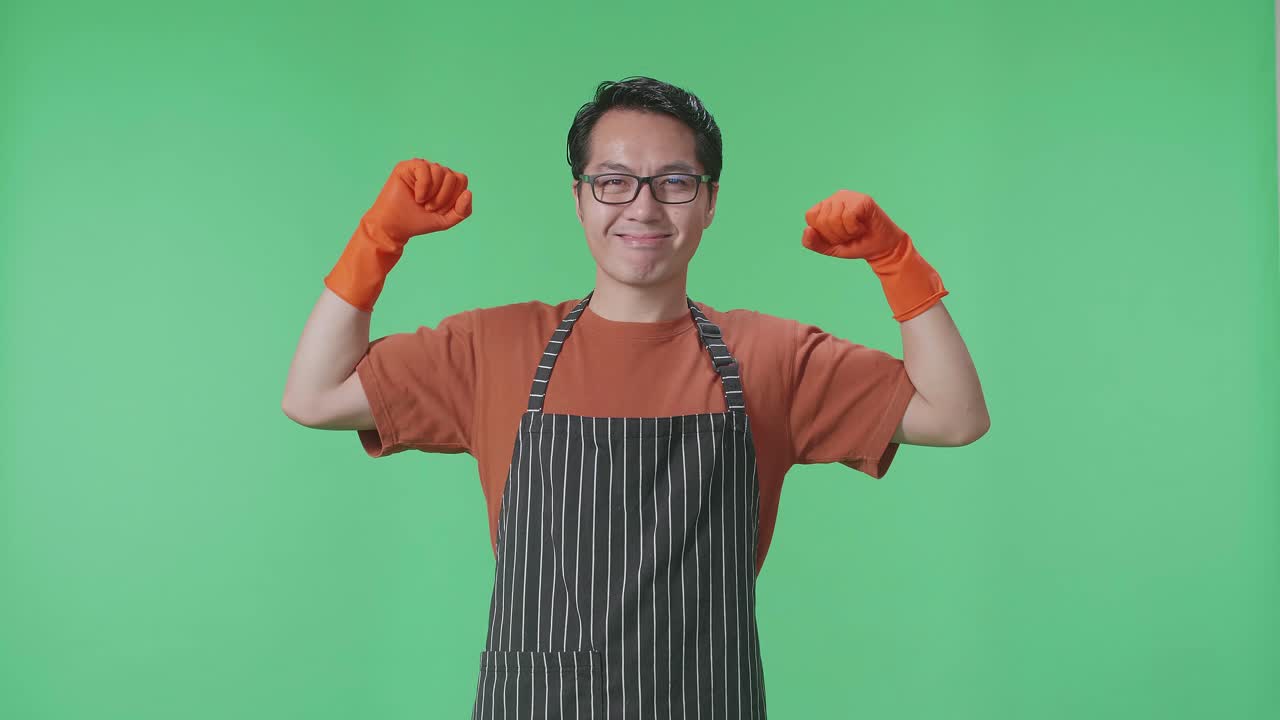 초록색 스크린 스튜디오에 서 있는 동안 그녀의 비셉스를 보여주는 아프론을 입은 아시아 남성 집주인