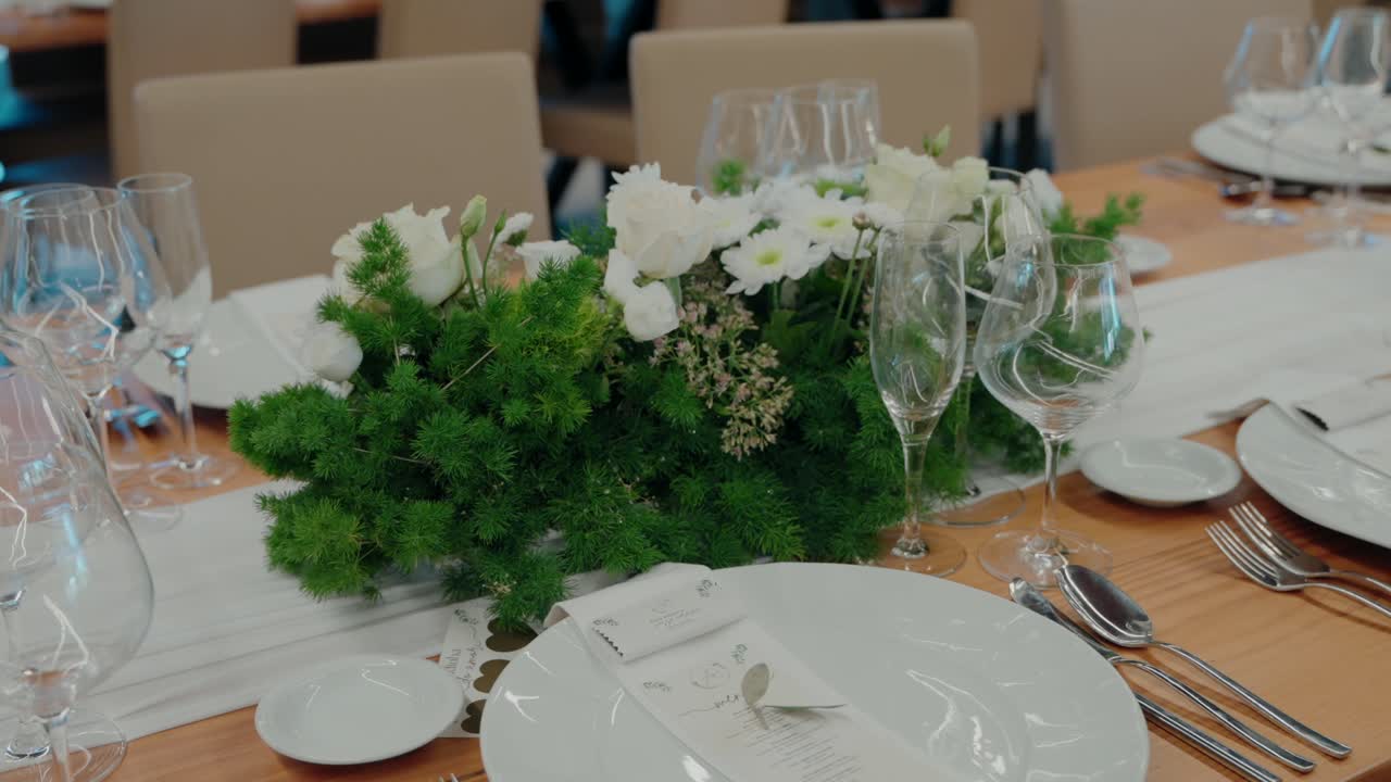White flowers and green foliage decorate a wedding table with glassware