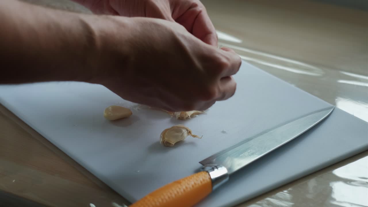 Removing garlic skin by hand after crushing with knife on cutting board.